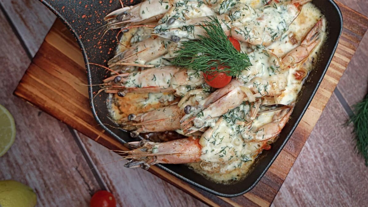 Sautéed shrimp in creamy sauce with dill and cherry tomatoes in an iron skillet.