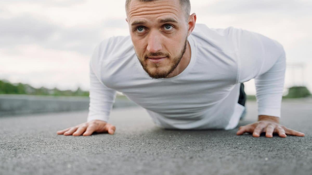 A man in a white shirt performs push-ups on an outdoor surface, focusing on fitness.