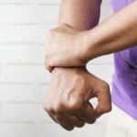 Close-up of a person holding their wrist in pain against a brick wall background.
