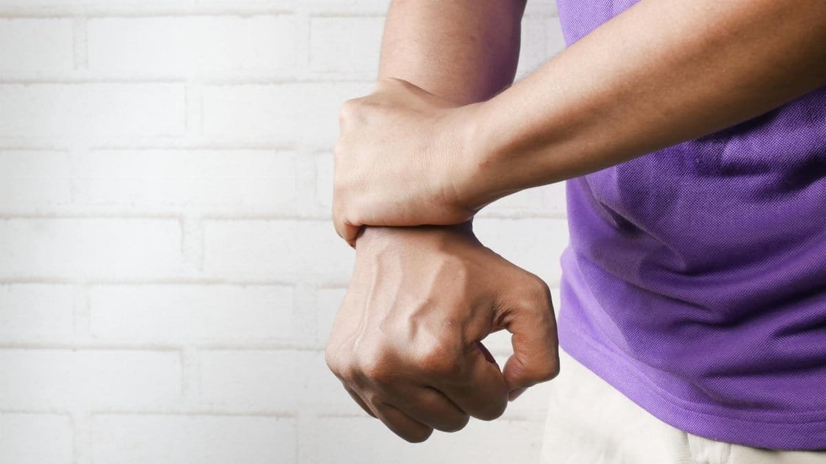Close-up of a person holding their wrist in pain against a brick wall background.
