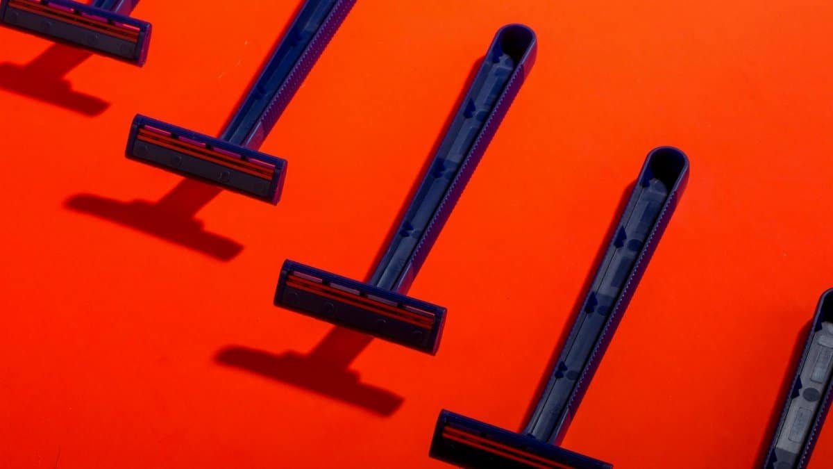 Blue disposable razors arranged neatly on a vivid orange background, creating a striking contrast.