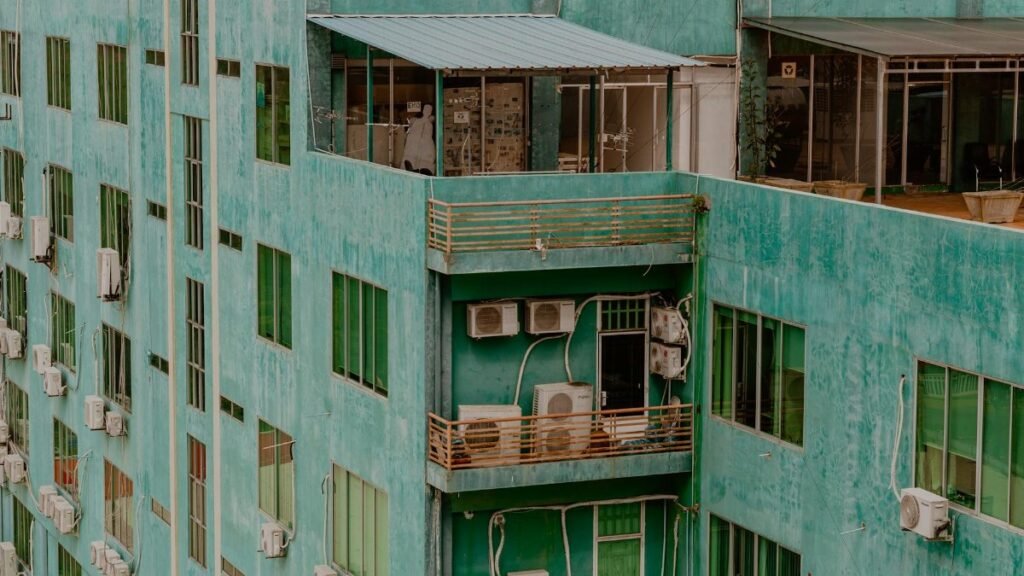 Detailed photo of a green apartment building with balconies and air conditioning units, captured from above.