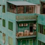 Detailed photo of a green apartment building with balconies and air conditioning units, captured from above.