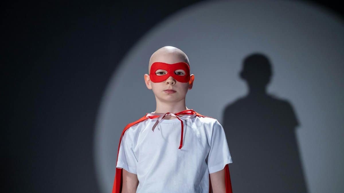 Portrait of young superhero in a white shirt, red cape, and mask with a bold shadow behind.