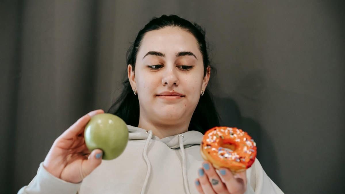 A young woman ponders a healthy apple versus a tempting donut. Lifestyle choice dilemma.