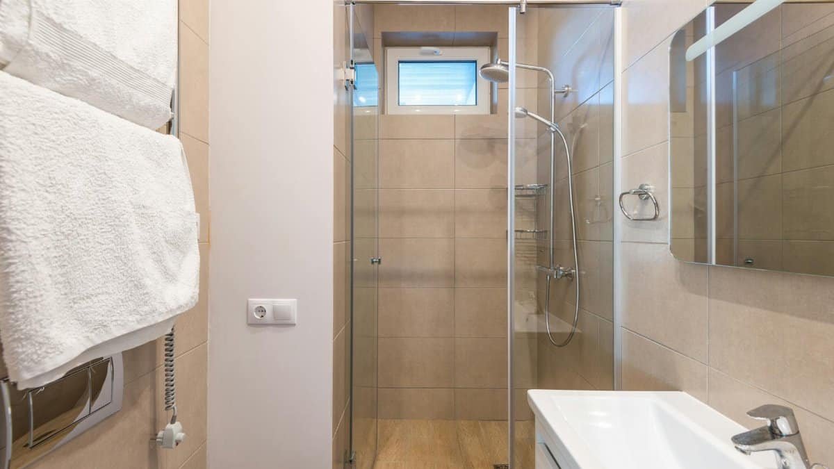 Contemporary bathroom featuring a glass shower, beige tiles, and a sleek sink area.