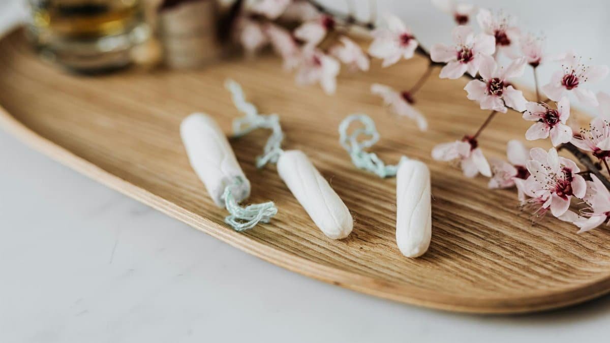 High angle of three menstrual tampons on bamboo plate with flower twig placed against various cosmetic products
