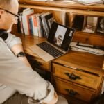 Senior man having a video call using a laptop at a wooden desk indoors.