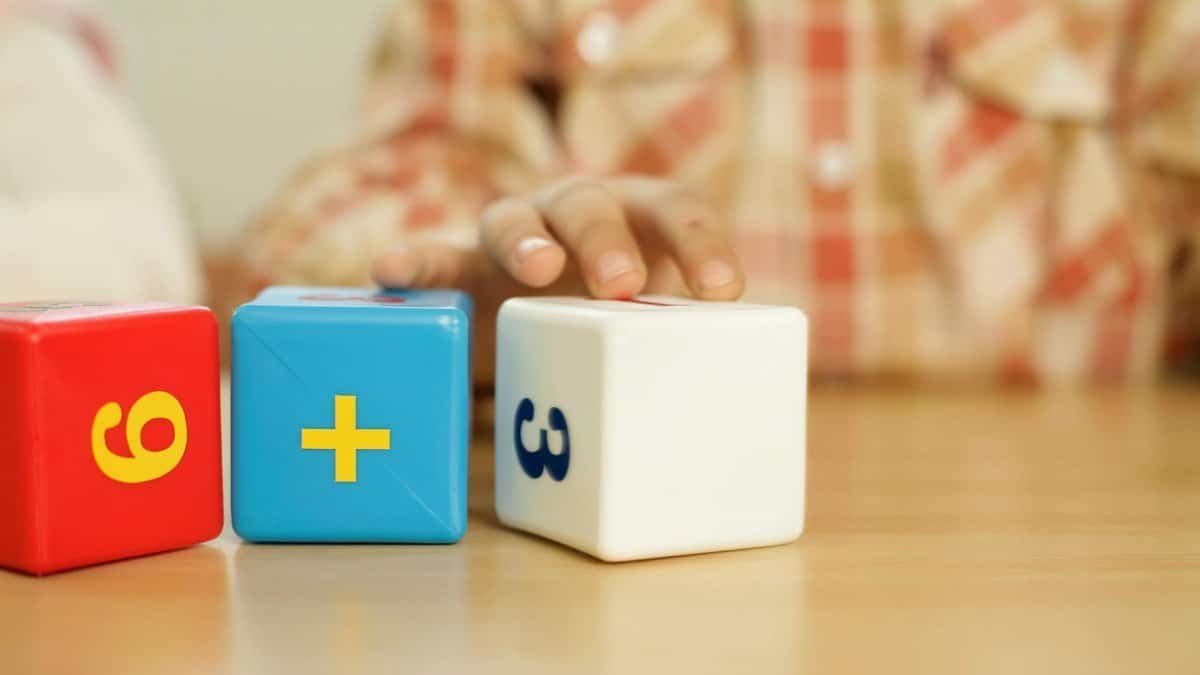 Close-up of child's hand touching educational math blocks on desk.
