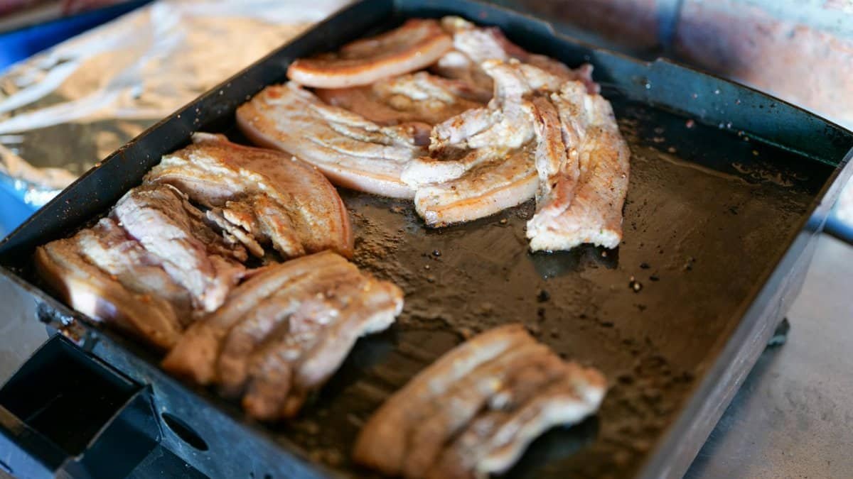 Close-up of succulent roasted pork belly slices sizzling on a grill pan, capturing the essence of Italian cuisine.