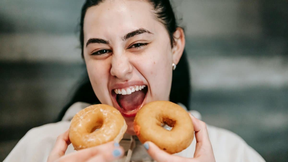 Smiling young woman indulging in tasty donuts at home.