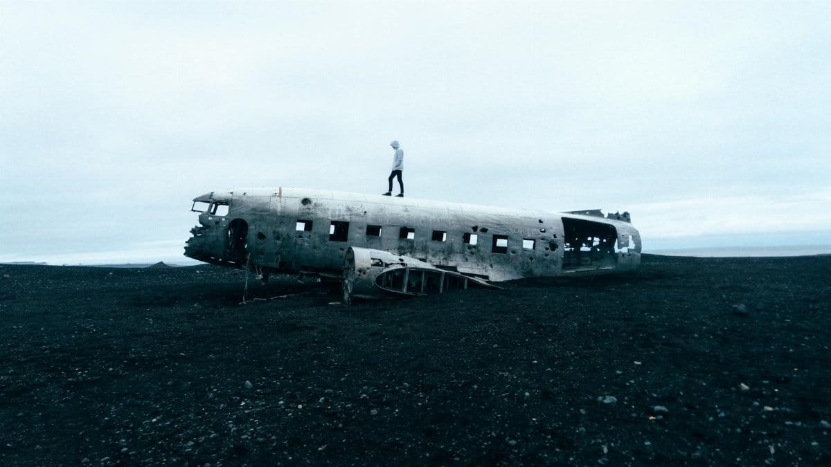 Eerie scene of an abandoned plane wreck on Icelandic beach with a person standing on top.