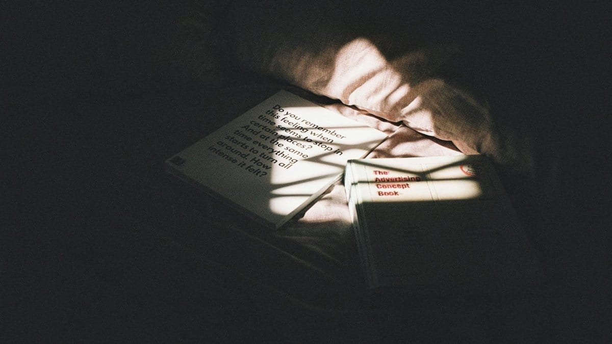 Moody image of books on a bed, illuminated by sunlight and shadows.