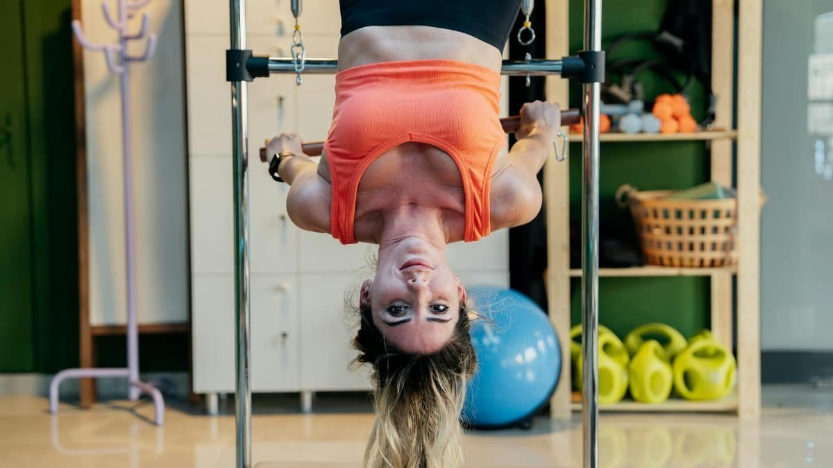 Woman practicing inverted Pilates on a reformer at a gym, focused on fitness and flexibility.