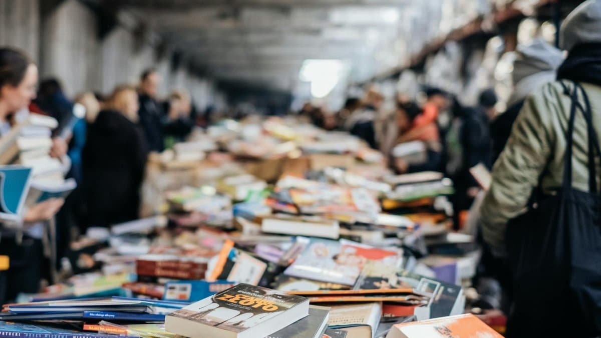 A bustling indoor book sale with numerous books and diverse people browsing.