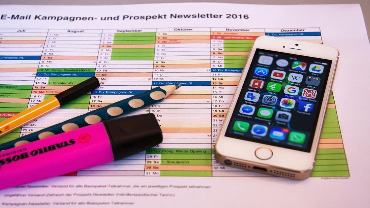 A desk setup featuring a planner, pens, and a smartphone displaying app icons, ideal for productivity.