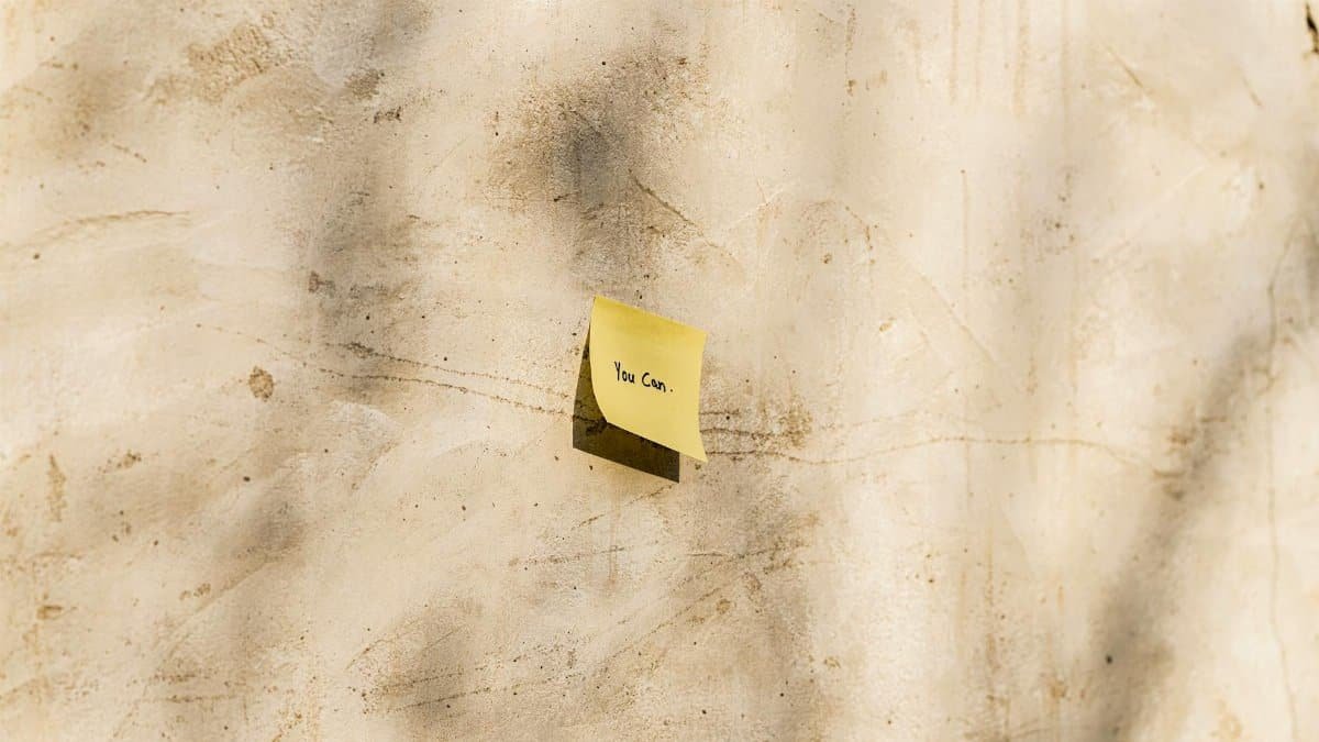 A yellow sticky note with 'You Can' written, placed on a textured outdoor wall.