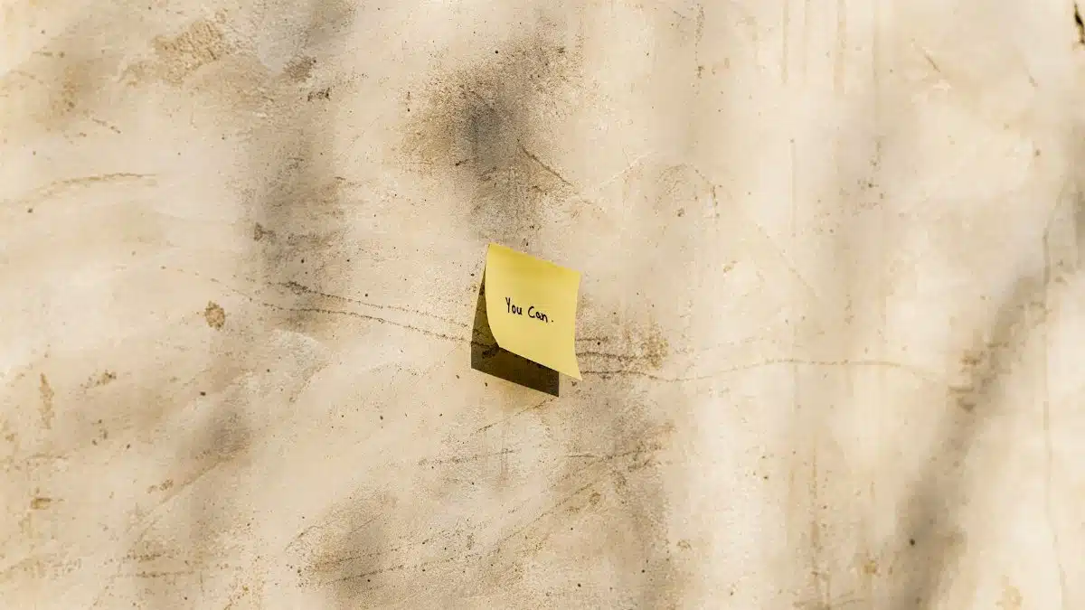 A yellow sticky note with 'You Can' written, placed on a textured outdoor wall.