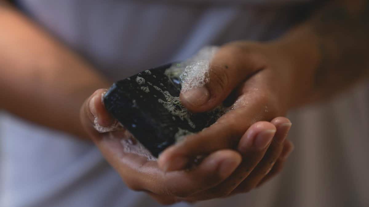 Detailed image of hands washing with black bar soap, capturing bubbles and texture.