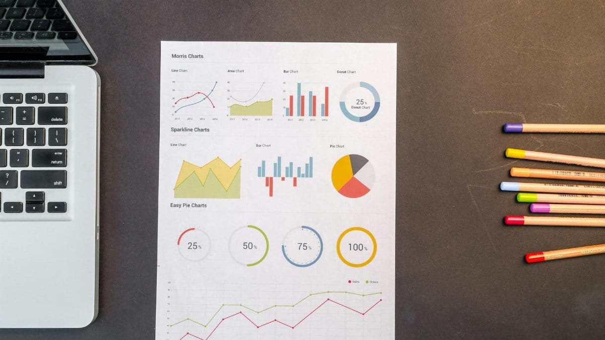 Top view of charts and colored pencils on a desk next to a laptop, perfect for business or education themes.