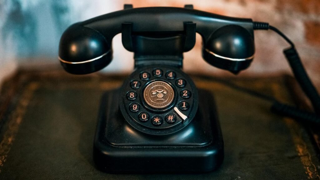 Classic black rotary dial phone on an antique table in a vintage setting.