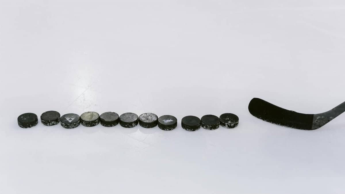 A row of hockey pucks and a stick on an ice rink, perfect for sports content.