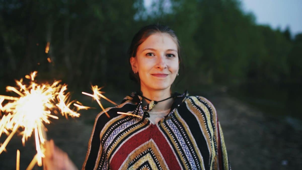 A young woman with a sparkler smiles outdoors, creating a joyful atmosphere.