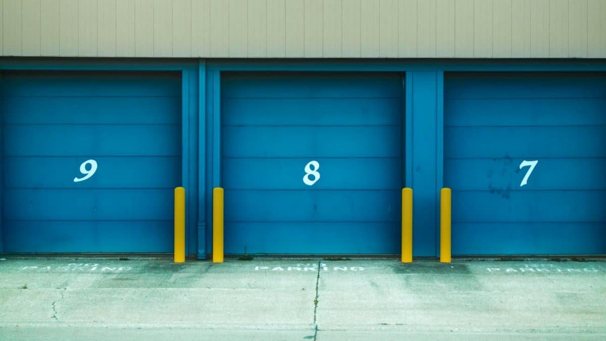 Three blue shutter doors numbered 9, 8, and 7 with yellow barriers in urban environment.