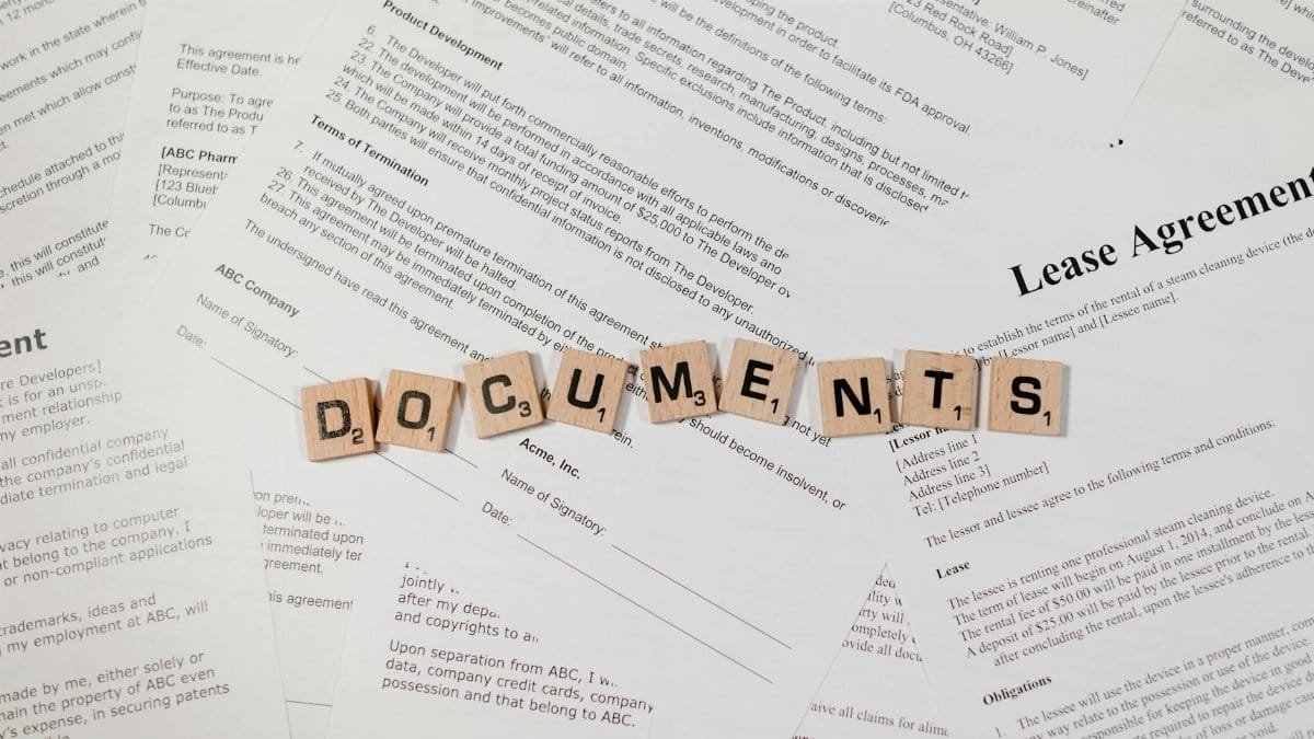 Top view of scrabble tiles spelling 'DOCUMENTS' on various contracts and agreements.