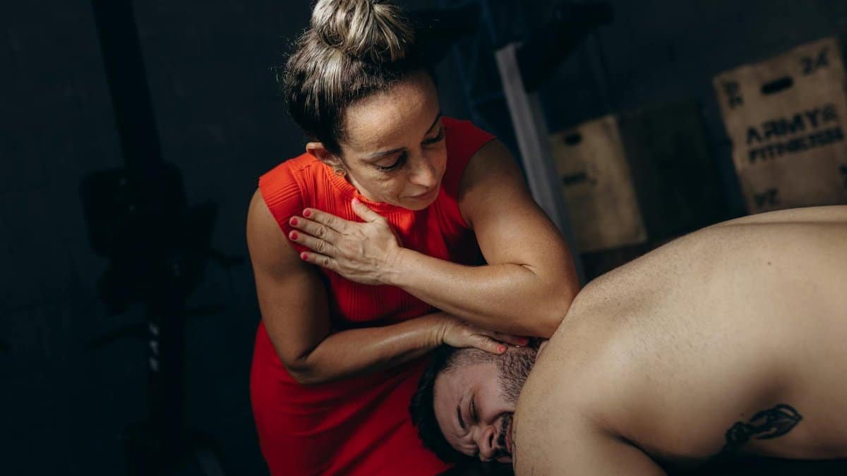 A therapist in red dress conducts a myofascial release session on a male client, aiding recovery.