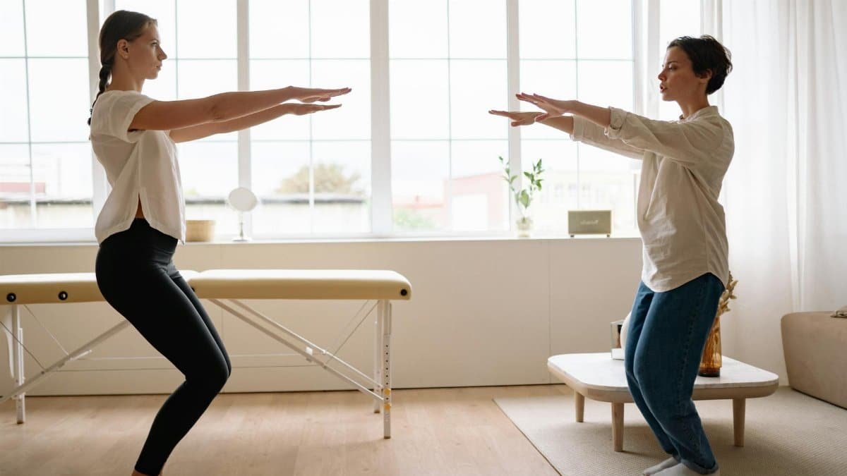 Two women practicing yoga together in a bright, airy room, focusing on fitness and wellness.