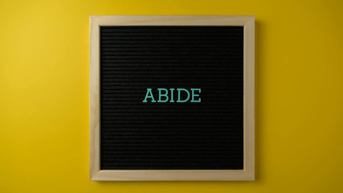 A black letter board with the word 'ABIDE' in teal on a vibrant yellow background, perfect for inspiration.