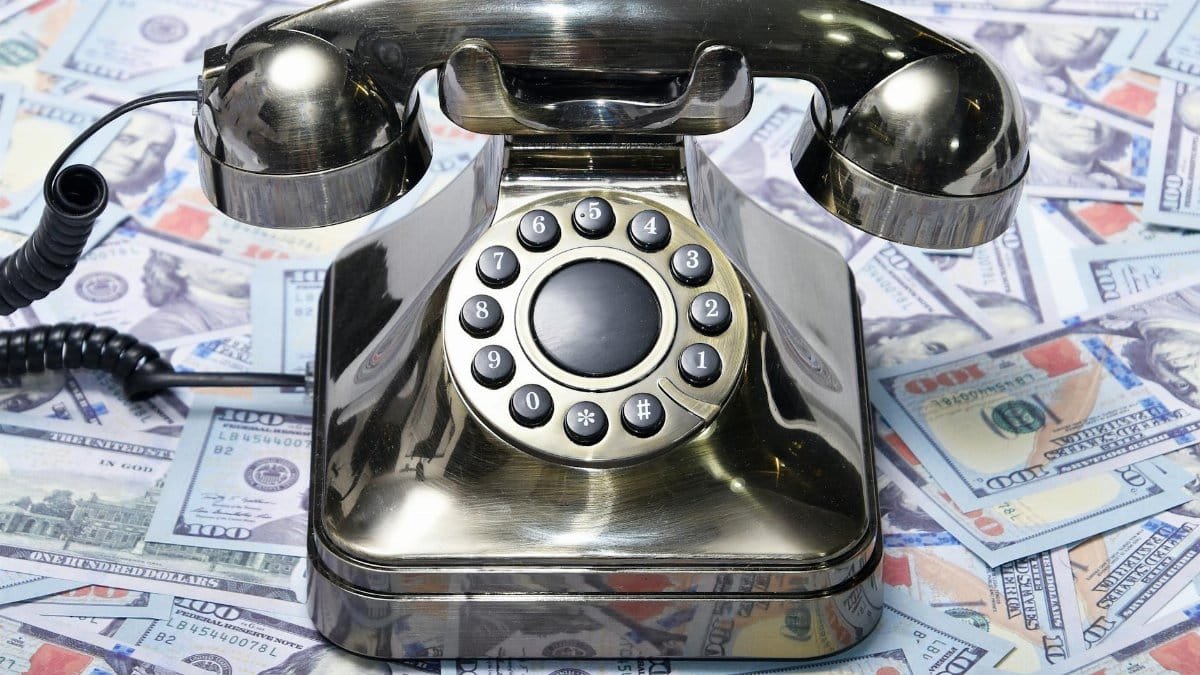 A retro rotary phone placed on a pile of US dollar bills, symbolizing communication and finance.