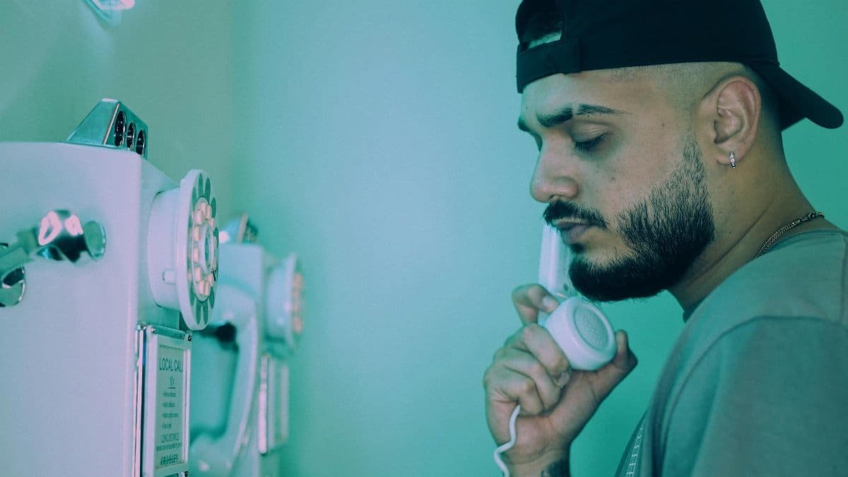 A bearded man in a cap using a vintage telephone with teal mood lighting.