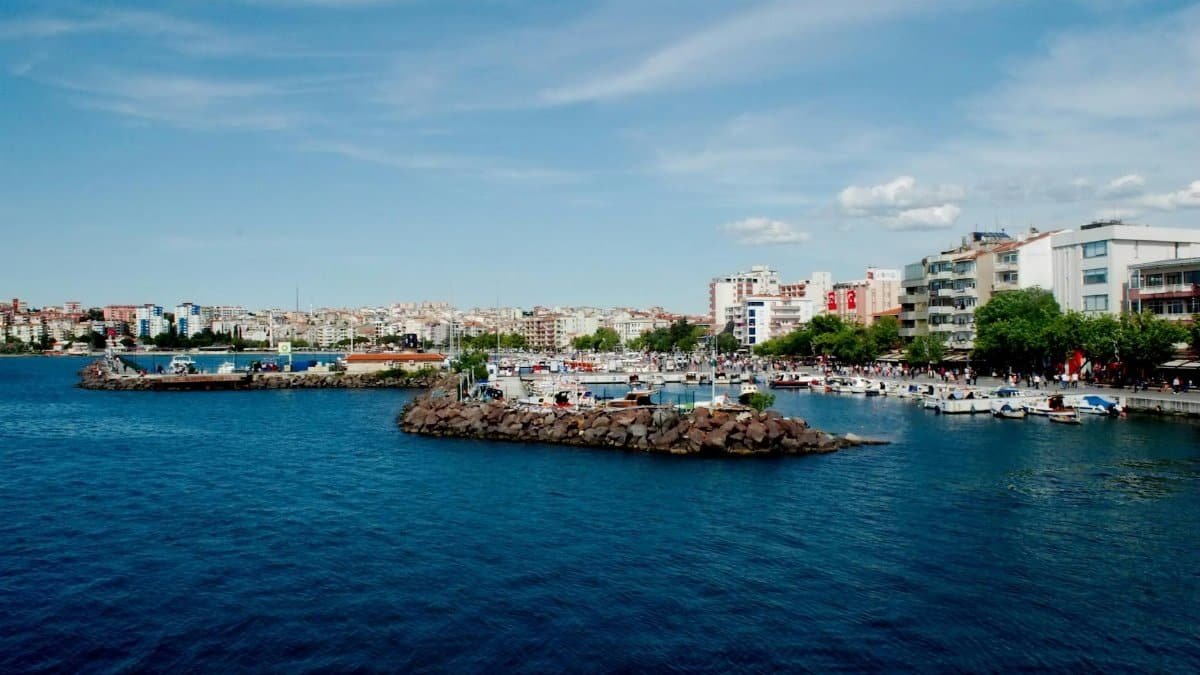 Explore the vibrant Çanakkale seascape with its bustling harbor and city skyline under a clear blue sky.