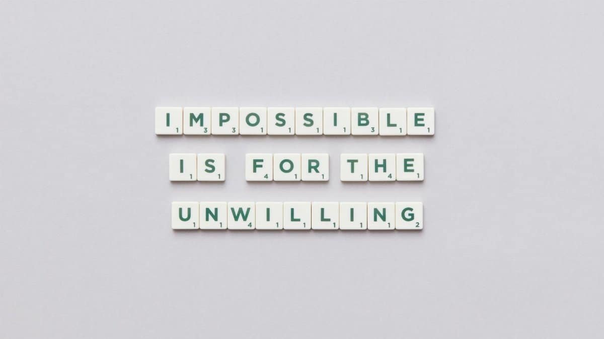 Inspirational quote 'Impossible is for the unwilling' made with letter tiles on a minimalist background.