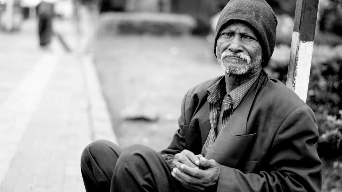 A black and white portrait of an elderly man sitting on the streets, expressing hardship and resilience.
