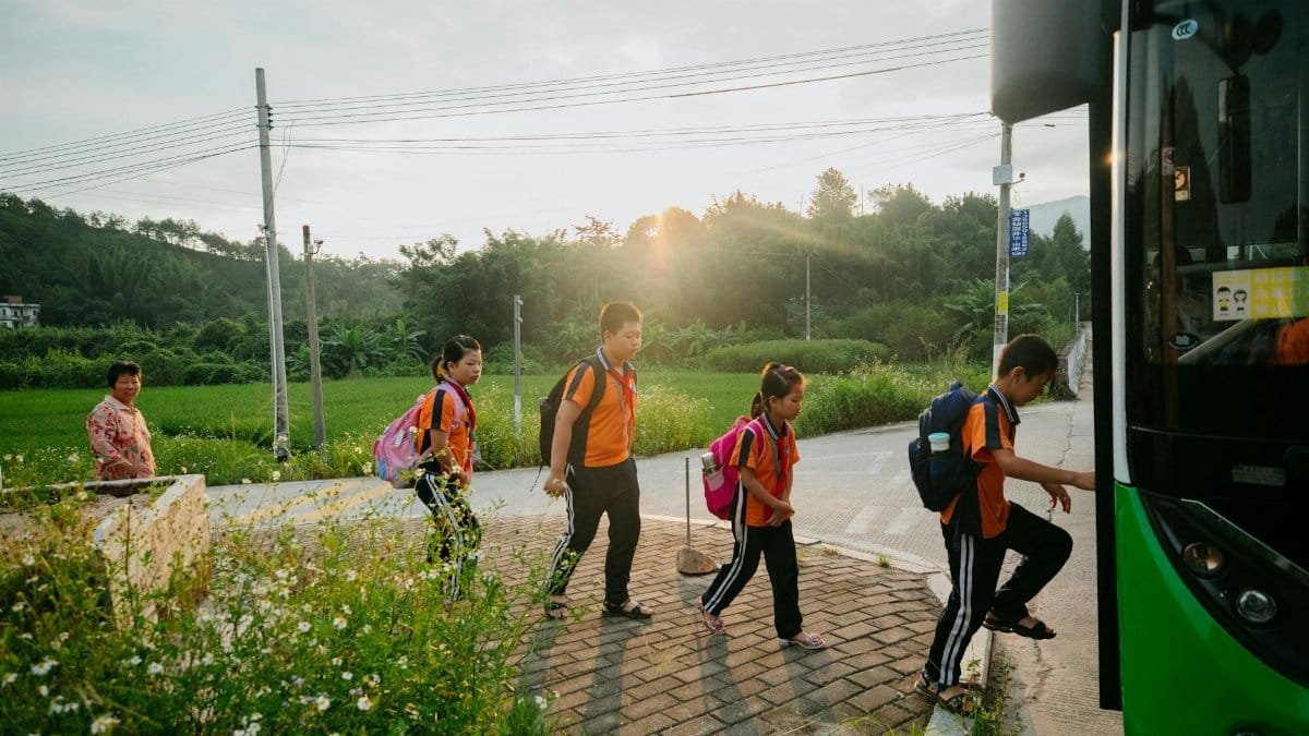 Group of Asian students in uniforms boarding a school bus at sunrise, showcasing a typical morning.