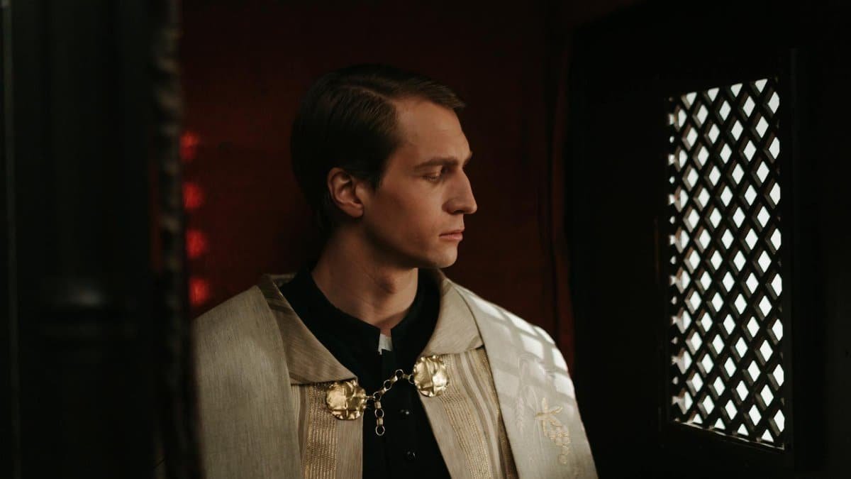 A priest in a traditional vestment sits in a confessional box, reflecting quietly.