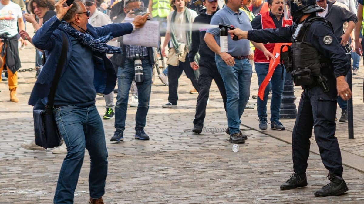 Intense protest scene in Bordeaux with police officer spraying demonstrator on crowded street.