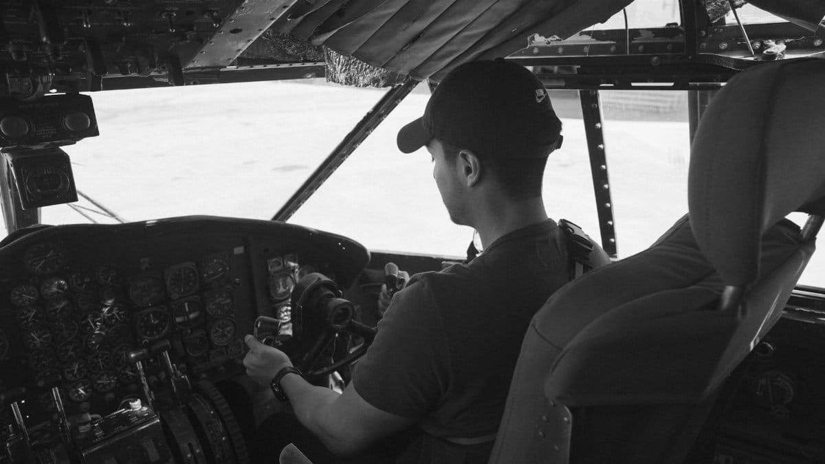 Monochrome photo of a pilot in an airplane cockpit, focusing on aviation controls.