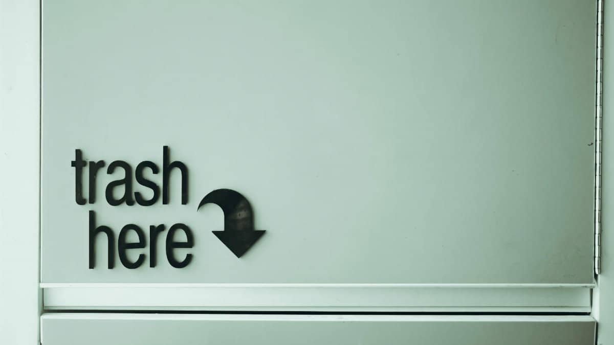 Black inscription with pointer indicating spot for trash disposal on white door of rubbish bin located in light public place