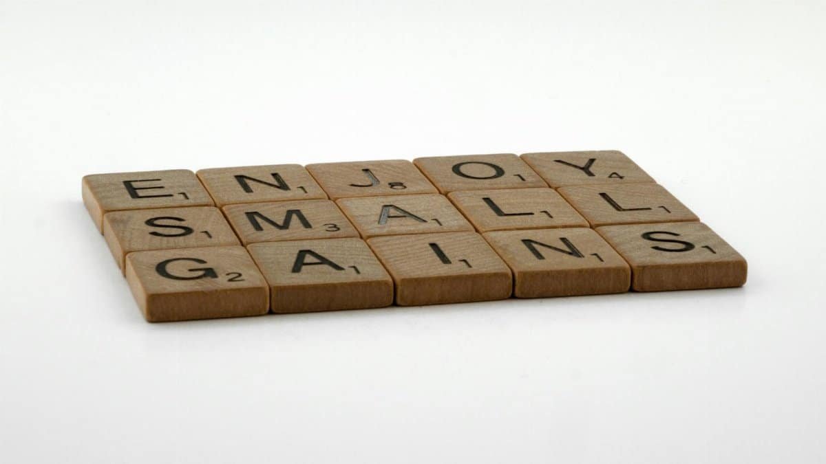 Close-up of Scrabble tiles forming the phrase 'Enjoy Small Gains' on a neutral background.