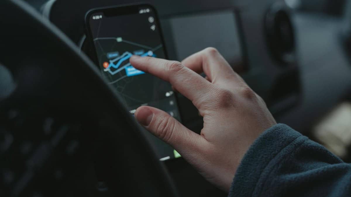 Hand interacting with GPS navigation on a smartphone mounted in a car interior.