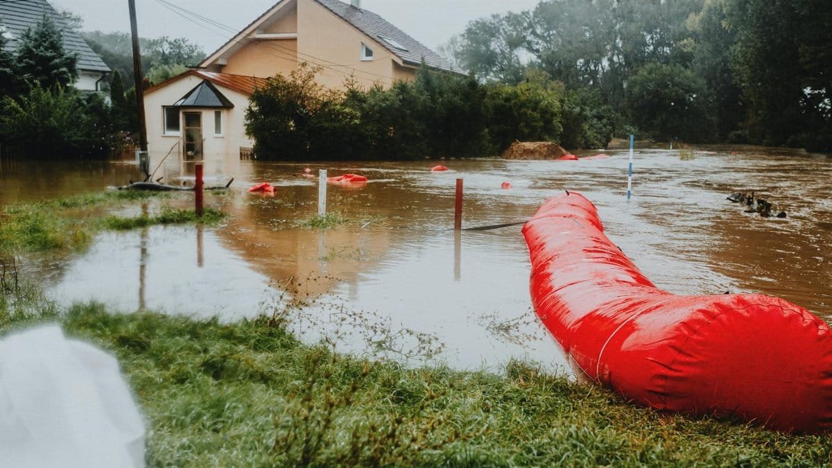 Flooded residential area protected by red flood barriers, showing severe weather impact.