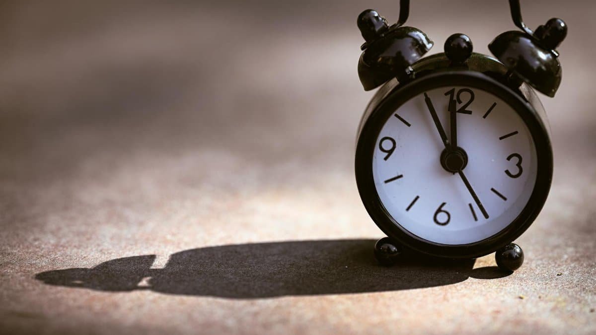 A classic black alarm clock showing five minutes to twelve on a textured surface with dramatic shadow.