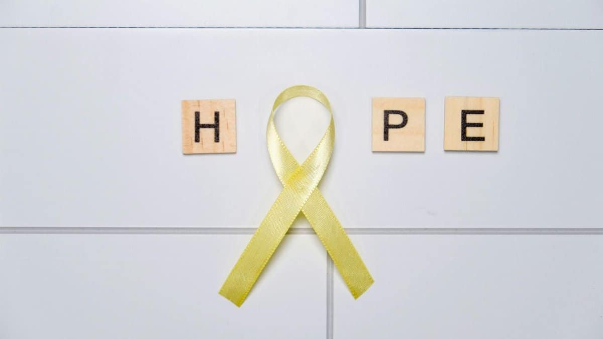 Yellow awareness ribbon forming 'O' with HOPE on tiles, symbolizing support and positivity.