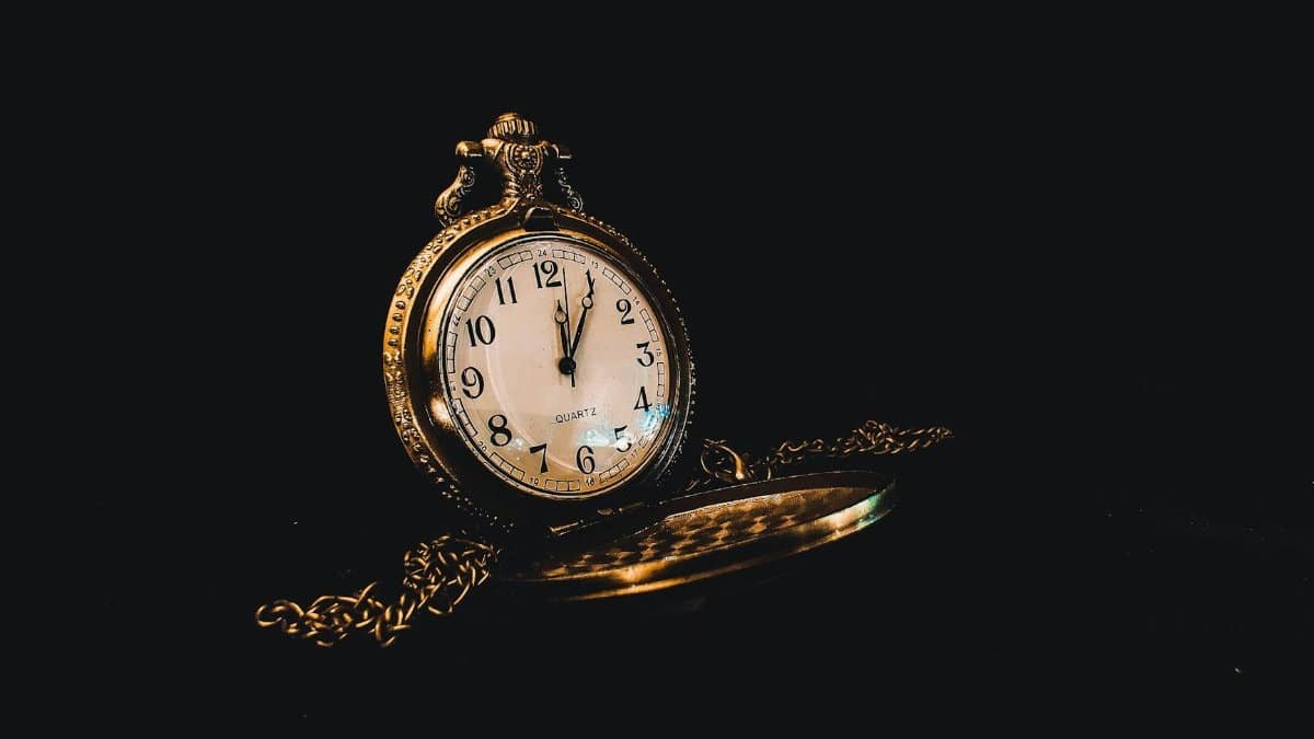 Classic vintage pocket watch with ornate design and chain on a dark background.