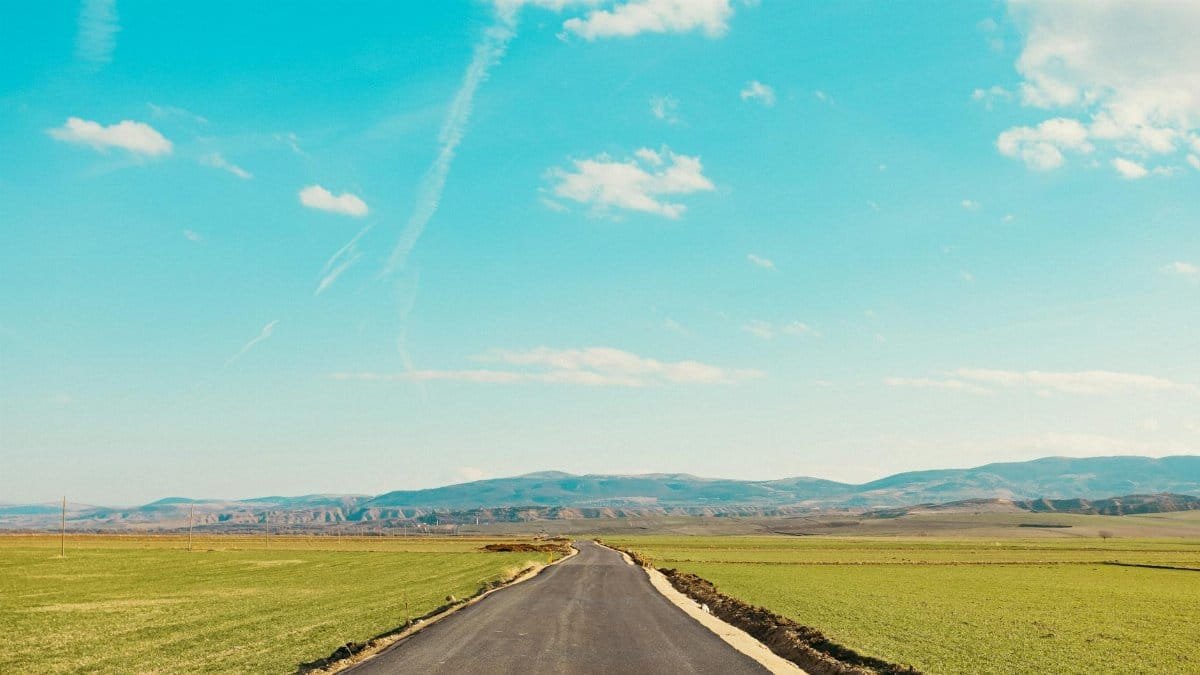 A serene countryside view with a paved road leading towards distant mountains.