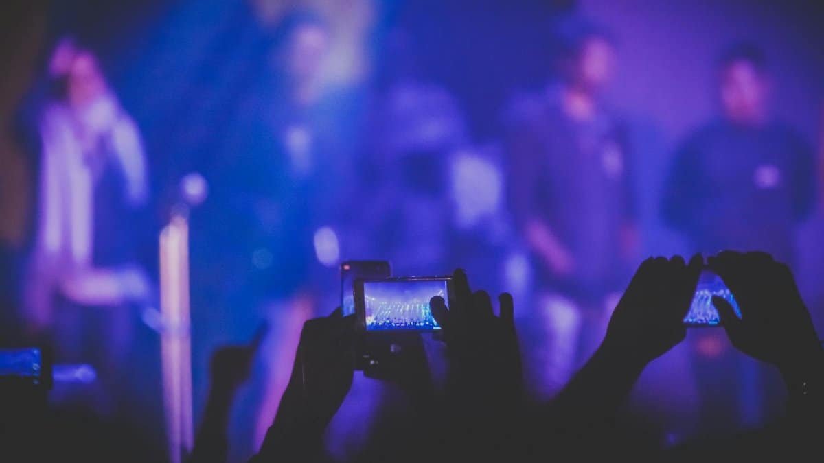 A lively concert audience capturing the show with smartphones under vivid stage lights.
